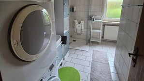 Ein kleines Badezimmer mit Waschmaschine, Trockner, einer Duschkabine aus Glas und einem Fenster für natürliches Licht.