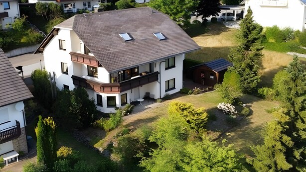 Ein modernes, zweistöckiges Haus mit schrägem Dach, zahlreichen Fenstern und einer kleinen angebauten Garage.