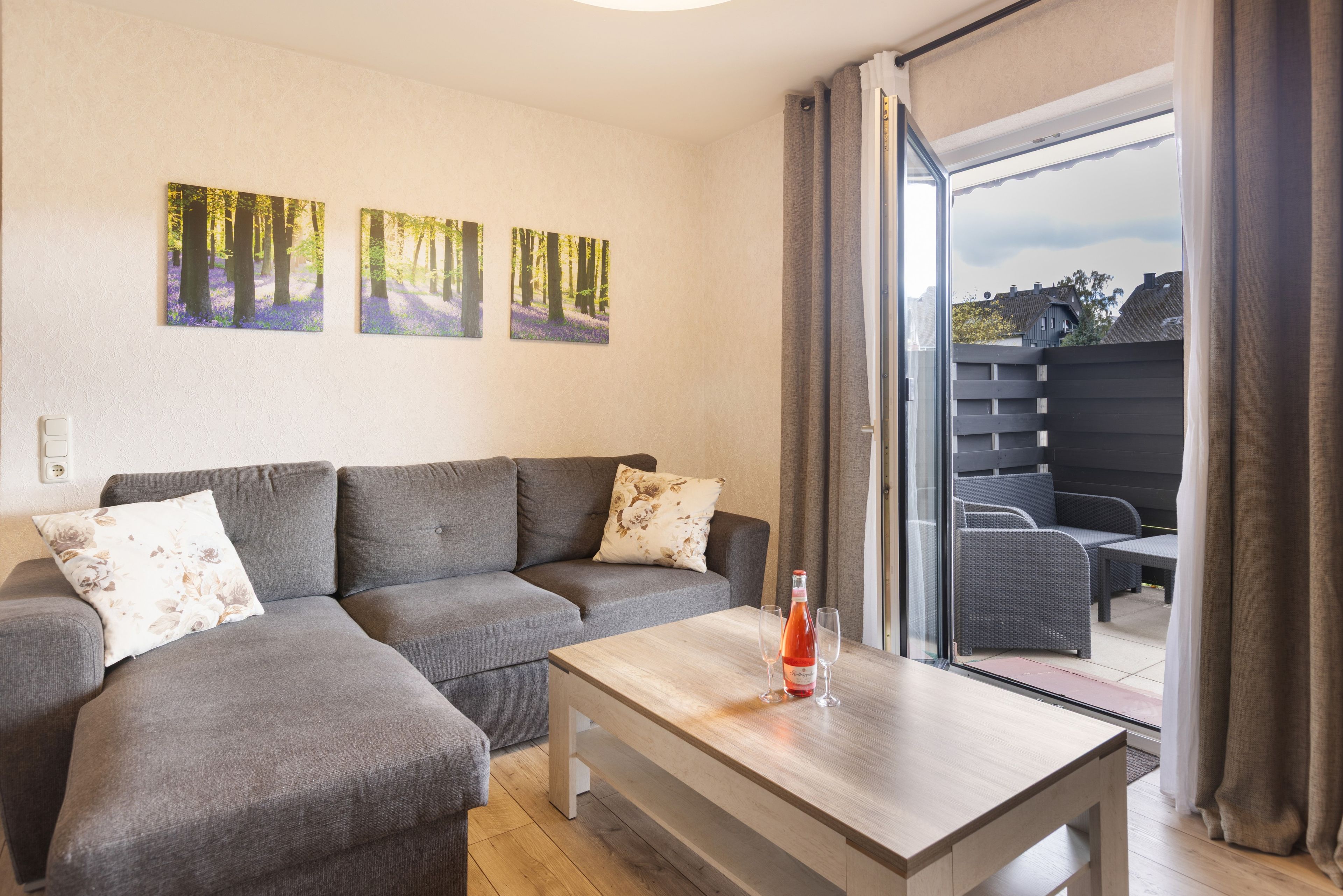 A modern living room with a grey sectional sofa, a wooden coffee table, and a view of a backyard through a sliding glass door.
