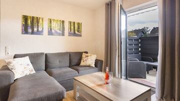 Een moderne woonkamer met een grijze modulaire bank, een houten salontafel en uitzicht op een achtertuin door een schuifdeur.
