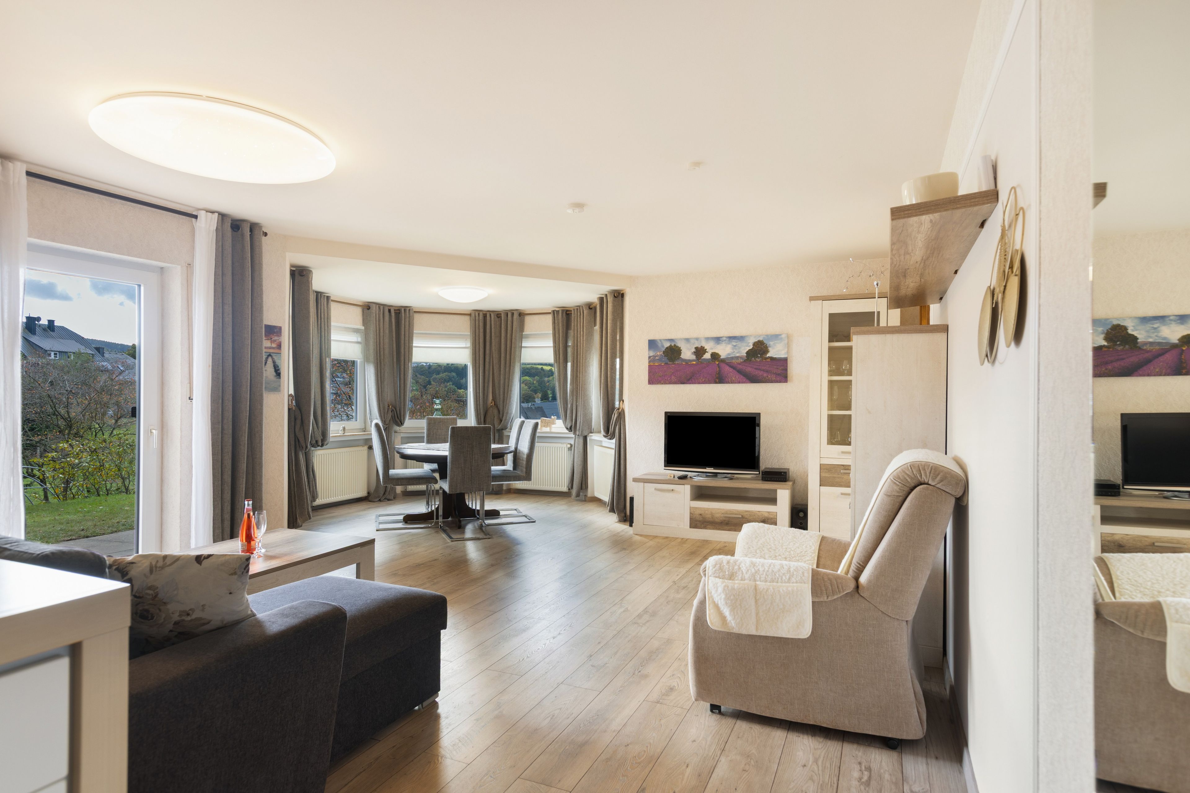 A modern living room with a sofa, a TV, and a dining area with a table and chairs.
