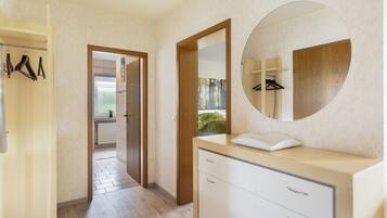 A modern bathroom with a wooden vanity, a round mirror, and a walk-in closet with hanging clothes.