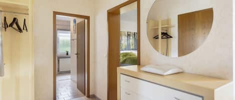 A modern bathroom with a wooden vanity, a round mirror, and a walk-in closet with hanging clothes.