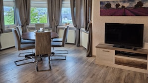 Ein Zimmer mit Esstisch, Stühlen, einem Flachbildfernseher und einem Bild an der Wand.