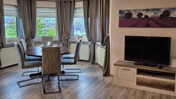 Een kamer met een eettafel, stoelen, een flatscreen televisie en een schilderij aan de muur.