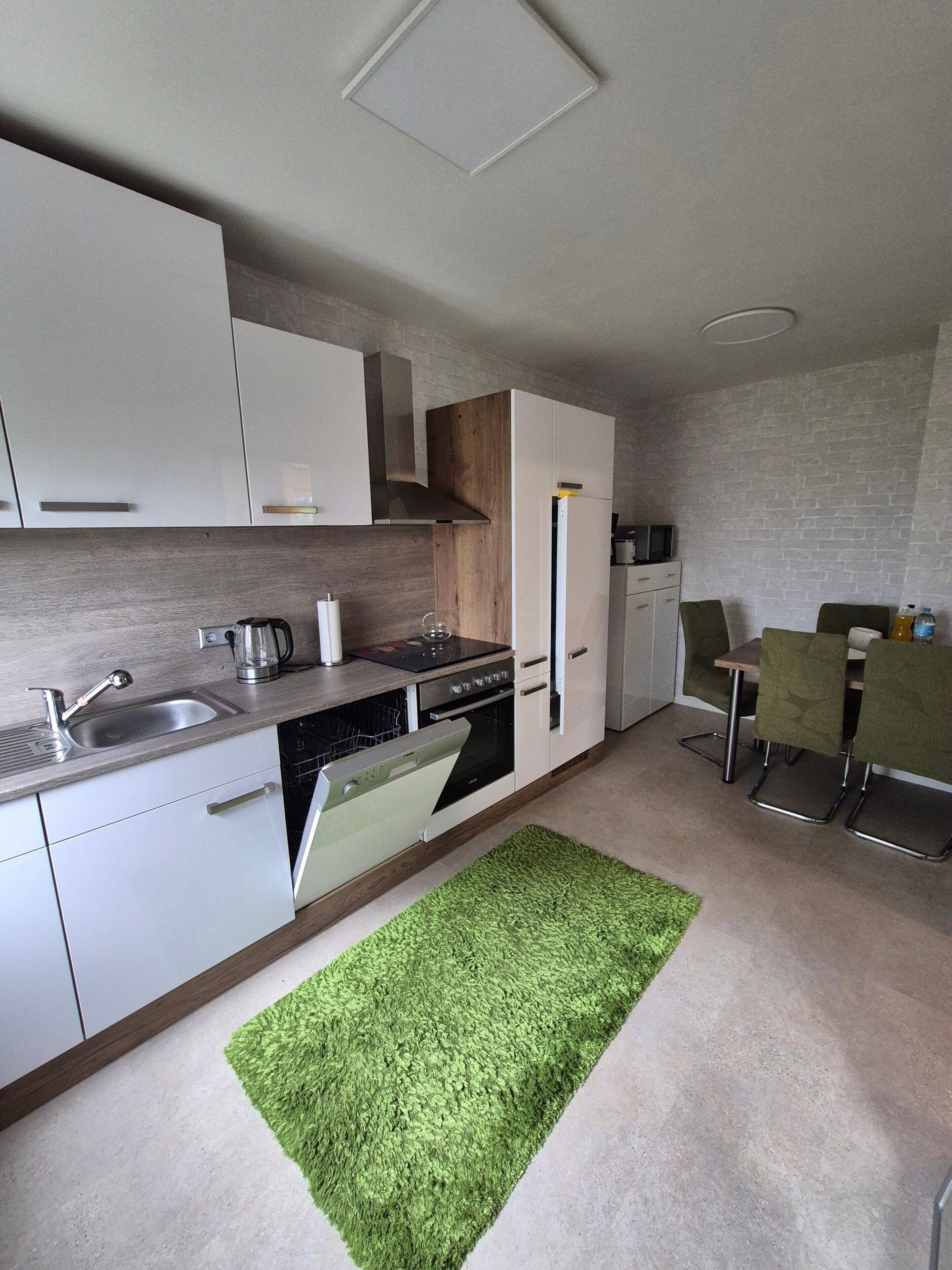 Una cocina moderna con armarios blancos, lavavajillas integrado y una alfombra verde.