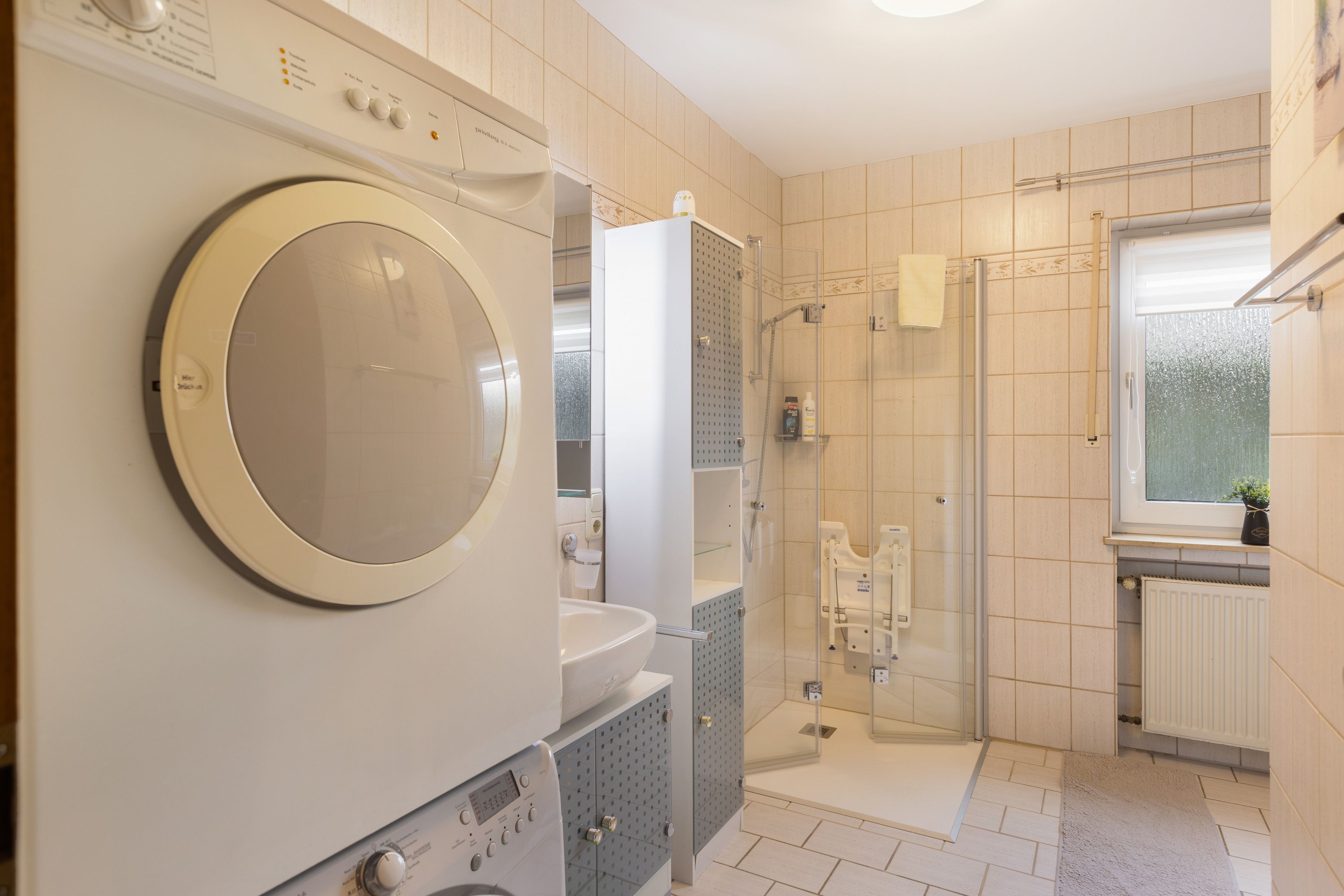 Ein modernes Badezimmer mit eingebauter Waschmaschine und Trockner, einer Duschkabine aus Glas und einem Fenster mit Blick.