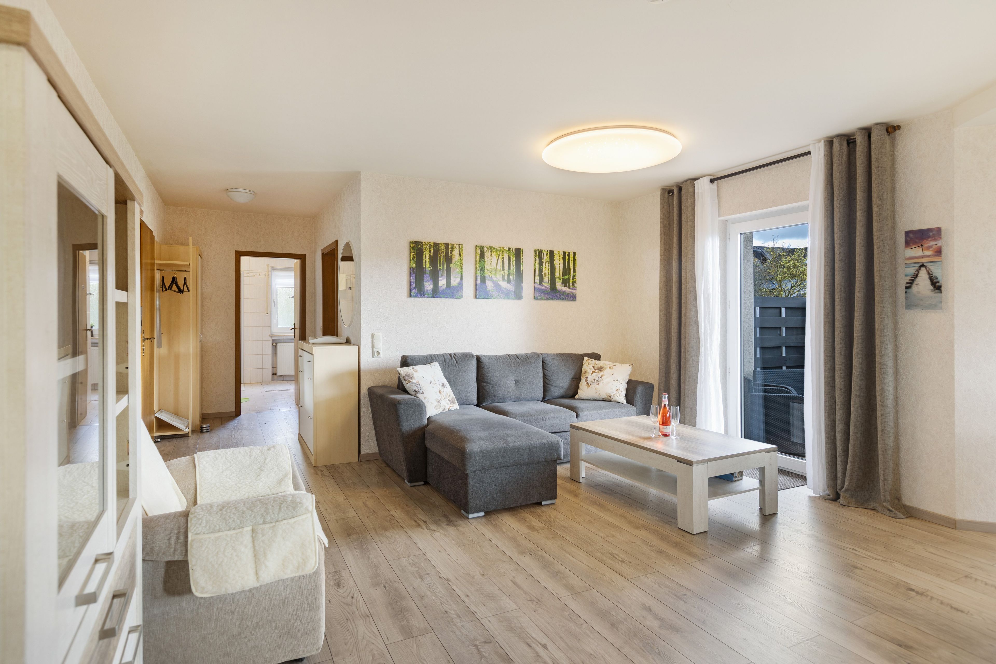 Ein modernes Wohnzimmer mit einem grauen Sofa, einem Couchtisch und Blick ins Freie durch eine Schiebetür.