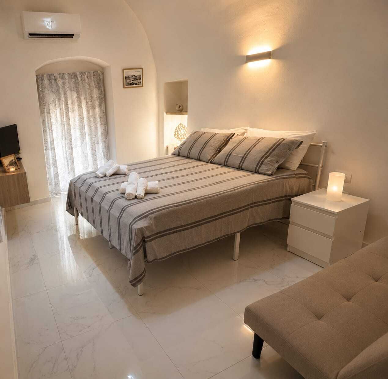 Ein Schlafzimmer mit einem Bett, Nachttischen, einer Lampe, einem Fernseher und einem Fenster mit Vorhängen.