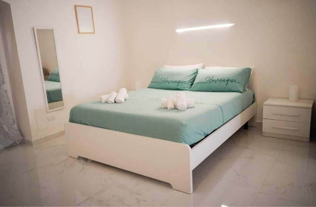 Ein ordentlich eingerichtetes Schlafzimmer mit Bett, Nachttisch, Spiegel und Wandleuchte.