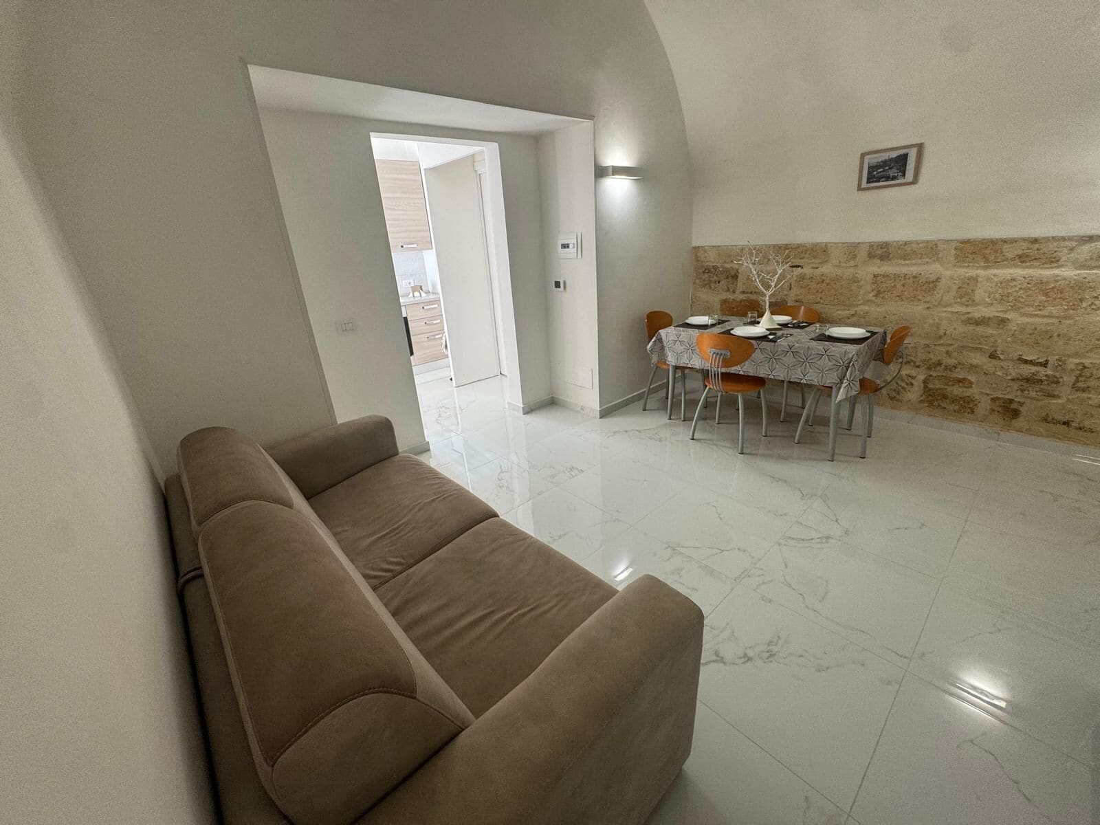 Un salon avec un canapé, une table à manger et des chaises, ainsi qu’un mur en pierre.