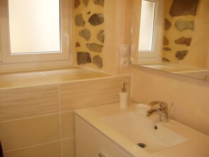 Une salle de bain avec un mur en pierre, une fenêtre, un lavabo et un miroir.
