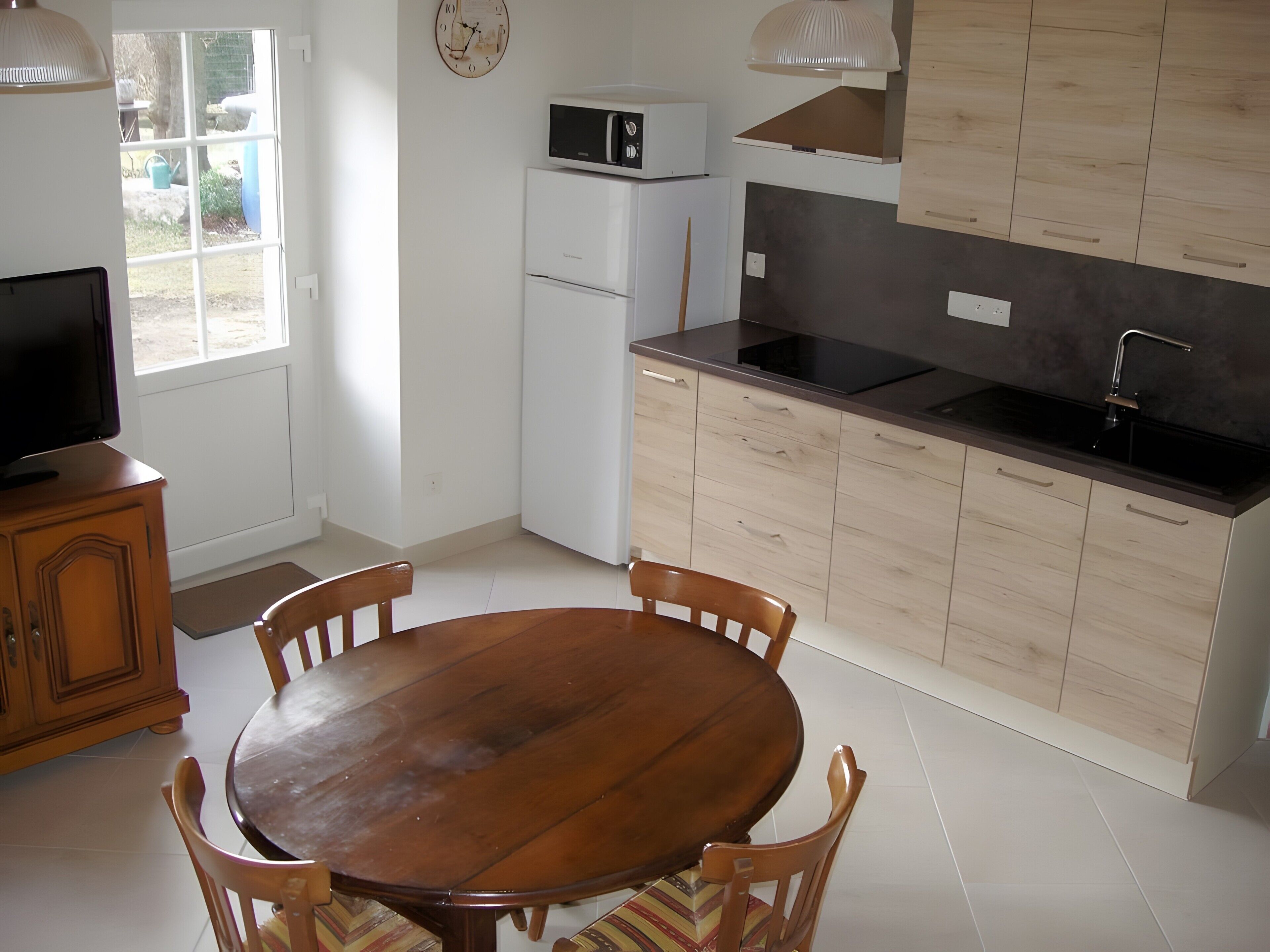 Una cocina con una mesa de madera, sillas, un microondas, un refrigerador y un lavamanos.