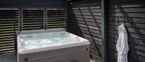 Un bain à remous avec un banc et une paire de chaussons, un porte-serviettes et une clôture en bois en arrière-plan.