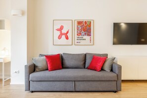 A grey sofa with red cushions, a framed artwork, and a television on the wall. - Pirandello 3 - Studio Apartment, Sleeps 4 (Milano)