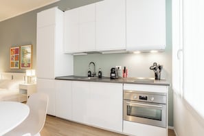 A modern kitchen with white cabinets, stainless steel appliances, and a dining area with a white table and chair. - Pirandello 3 - Studio Apartment, Sleeps 4 (Milano)