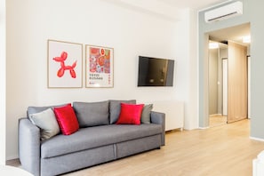 A modern living room with a grey sofa, red and grey cushions, a flat-screen TV, and two framed artworks on the wall. - Pirandello 3 - Studio Apartment, Sleeps 4 (Milano)