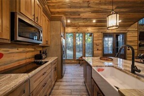 A kitchen with wooden cabinetry, a stainless steel microwave, and a large window. - IIII Pines + a Cone: Sleeps 18, Hot Tub, Game Room (Hochatown)