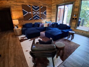 A cozy living room with a sectional sofa, a leather armchair, and a round wooden stool. - IIII Pines + a Cone: Sleeps 18, Hot Tub, Game Room (Hochatown)