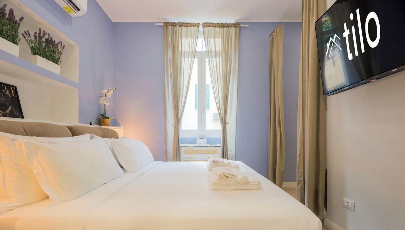 A hotel room with a bed, a television, a window with curtains, and a wall-mounted air conditioner.