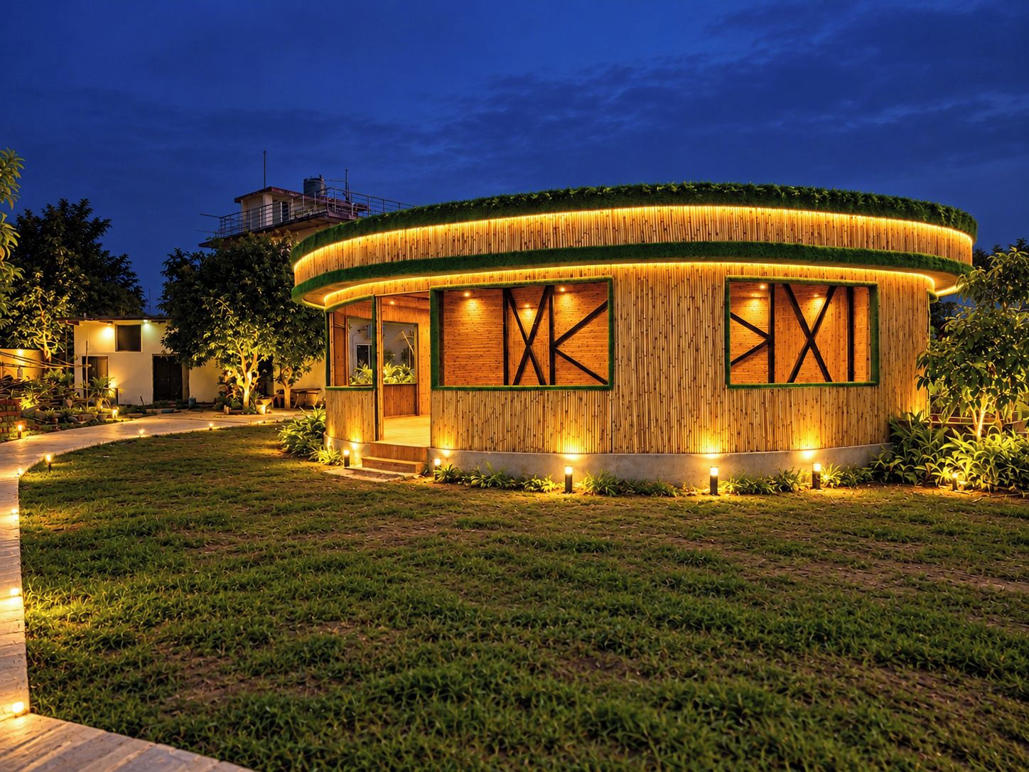A circular building with a wooden exterior and glass windows, surrounded by a well-lit lawn.