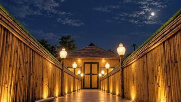 Un pasillo con estructura de madera, iluminado por farolas, que conduce a un edificio con una puerta verde.