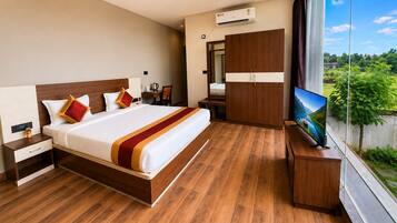 A modern hotel room with a wooden floor, a large bed with a red and white bedspread, a TV on a wooden stand, and a wardrobe.