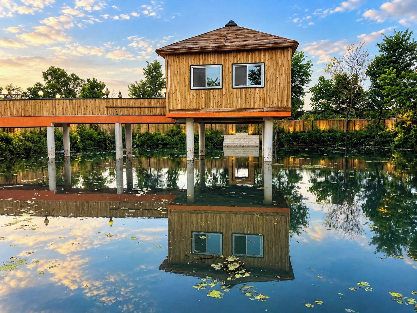 A wooden structure with a flat roof, supported by pillars, over a body of water with reflections.
