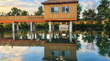 A wooden structure with a flat roof, supported by pillars, over a body of water with reflections.