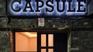 En byggnadsingång med en skylt som visar ordet ”CAPSULE” och en parkeringsförbudsskylt ovanför.