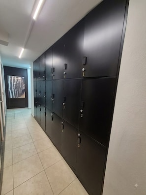 A hallway with a row of black lockers, numbered from 1 to 7, and a door with a zebra-striped design at the end. - CAPSULE (Ciudad de México)