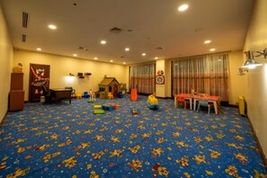 A room with a blue carpet featuring cartoon characters, a play area with toys, a small house, and a table with chairs.