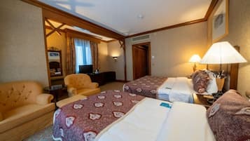 A hotel room with two beds, a sofa, a desk, and a television.