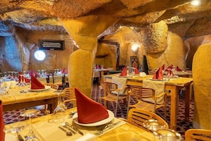 Ein unterirdisches Restaurant mit gedeckten Tischen, das durch eine höhlenartige Innenarchitektur mit natürlichen Felsformationen gekennzeichnet ist.