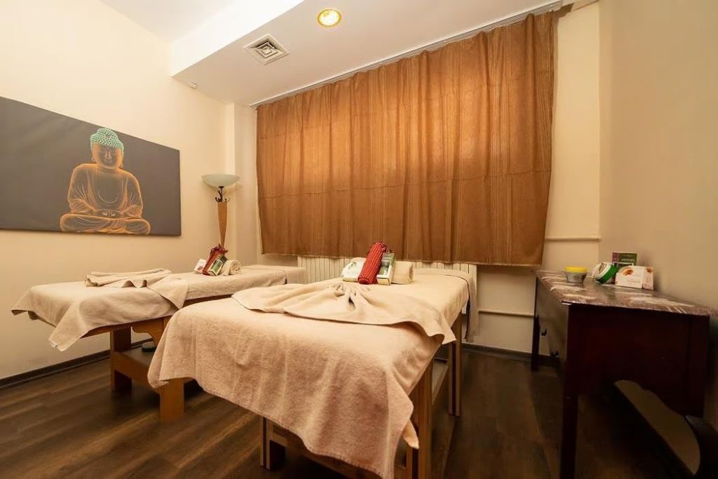 A room with two massage tables, a large Buddha statue, and a window with curtains.