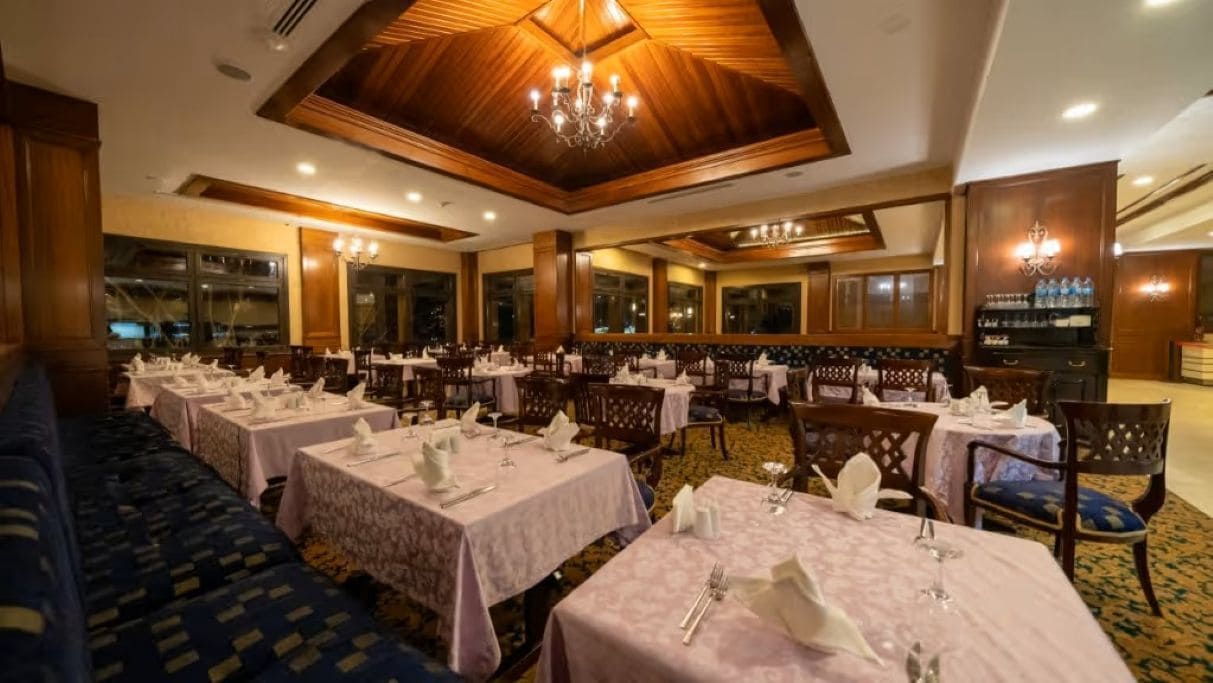 A restaurant with multiple tables set for dining, featuring a classic interior design with wooden paneling and chandeliers.