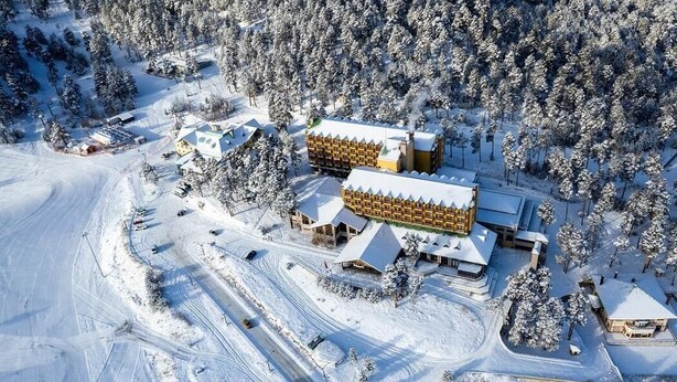 A snow-covered lodge with multiple buildings, a parking area, and a forested backdrop. - Erta Soyak Hotel Sarıkamış (Sarıkamış)