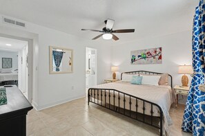 A bedroom with a bed, a ceiling fan, a painting, and a window with curtains. - 2-bedroom Cozy Beach Getaway w/ Screened Lanai (Madeira Beach)