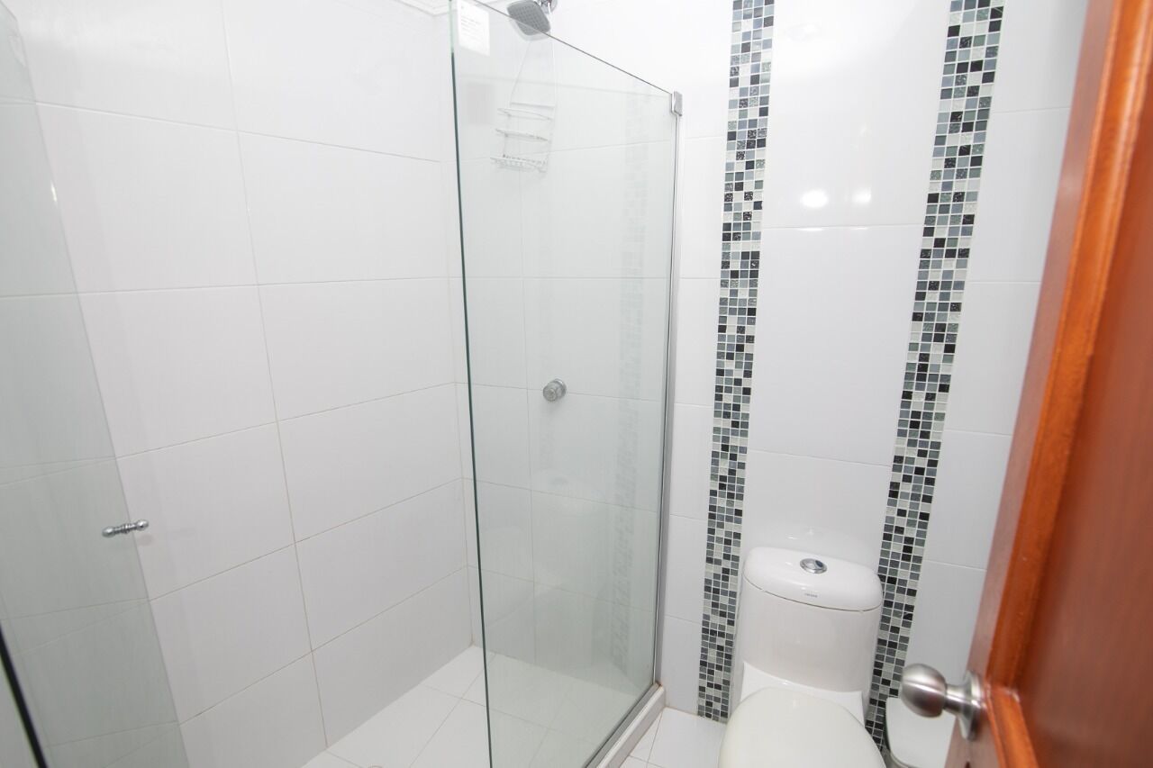 A bathroom with a glass-enclosed shower, white tiled walls, and a mosaic tile accent strip.