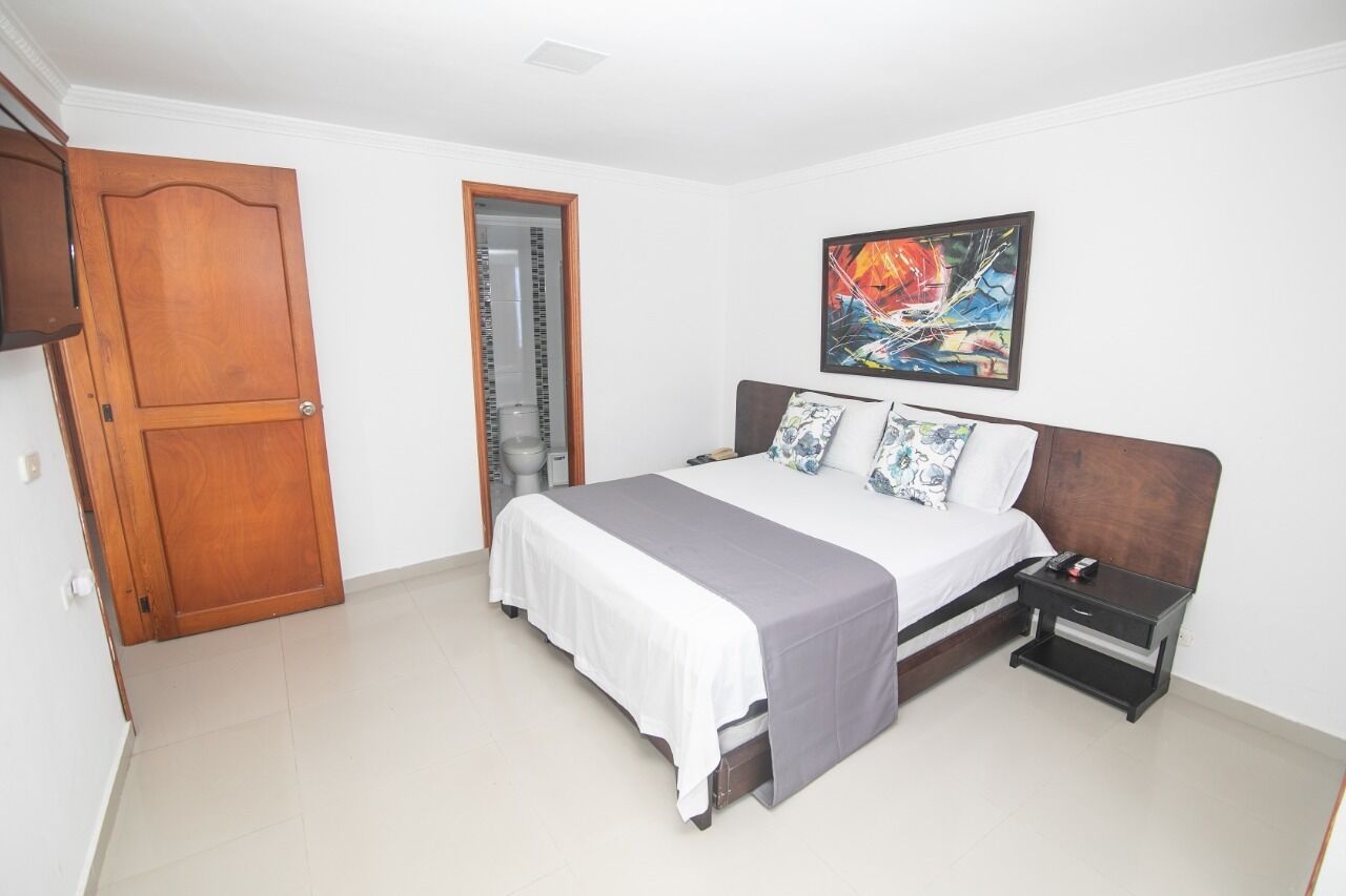 Un dormitorio con cama, mesita de noche, puerta de madera y un cuadro en la pared.