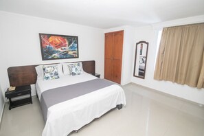 A bedroom with a bed, a nightstand, a wardrobe, a painting, and a window with curtains. - Vrbo Property (Cartagena de Indias)