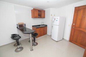 A compact kitchen with a microwave, a sink, wooden cabinets, a refrigerator, and two stools. - Vrbo Property (Cartagena de Indias)