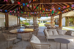 An outdoor patio area with round tables and wicker chairs, surrounded by colorful flags. - Beautiful apartment in Praia do Forte, near the best beach. (Mata de São João)