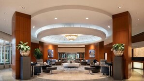 Eine moderne Lobby mit einer zentralen Sitzecke, einer Chandelier und großen Kübelpflanzen.