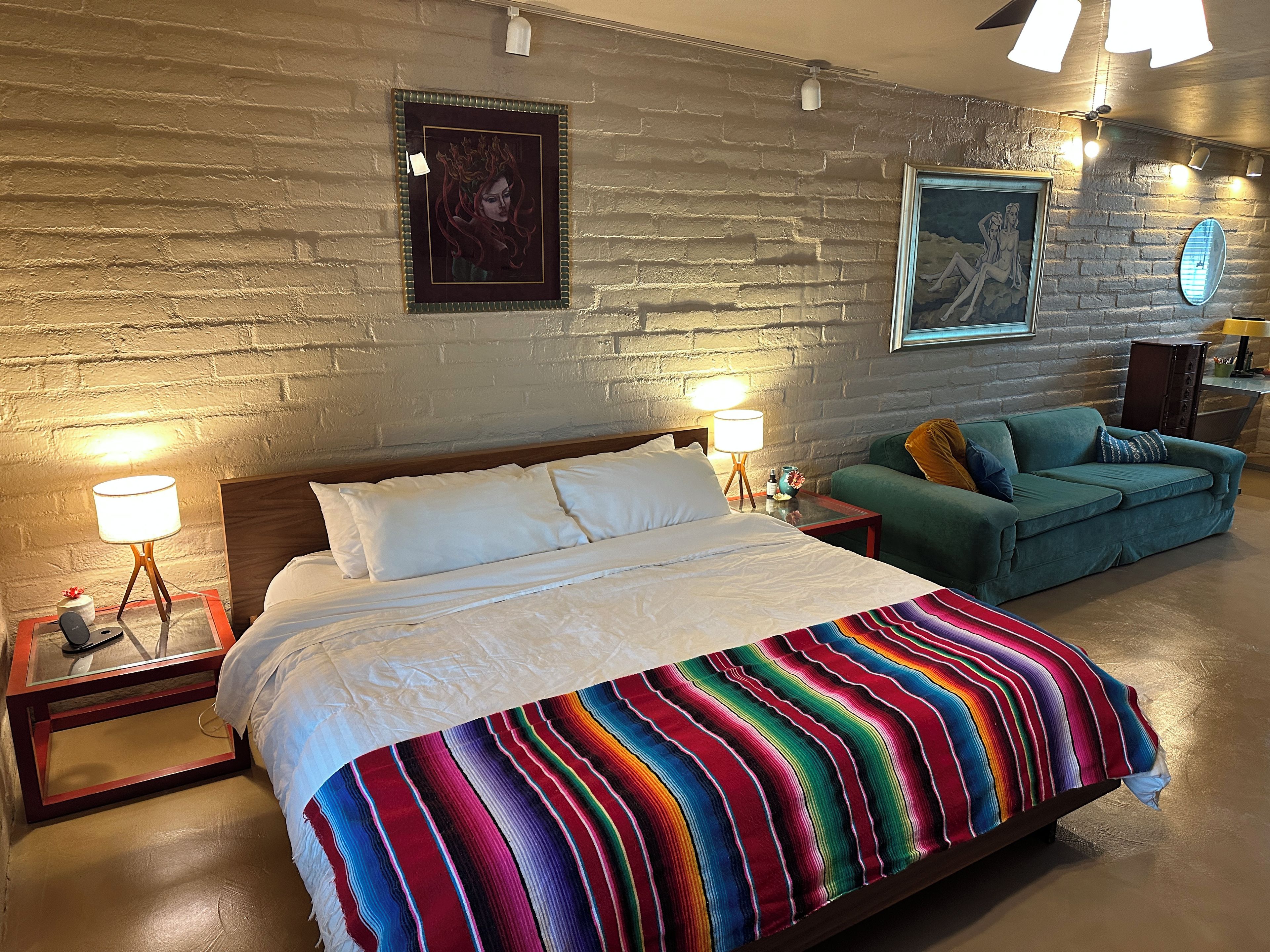 Une chambre d’hôtel avec un grand lit, un canapé vert et des œuvres d’art accrochées aux murs.