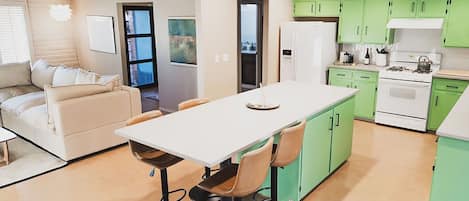 Una cocina moderna con gabinetes verdes, una encimera blanca y una zona de comedor con una mesa y sillas.