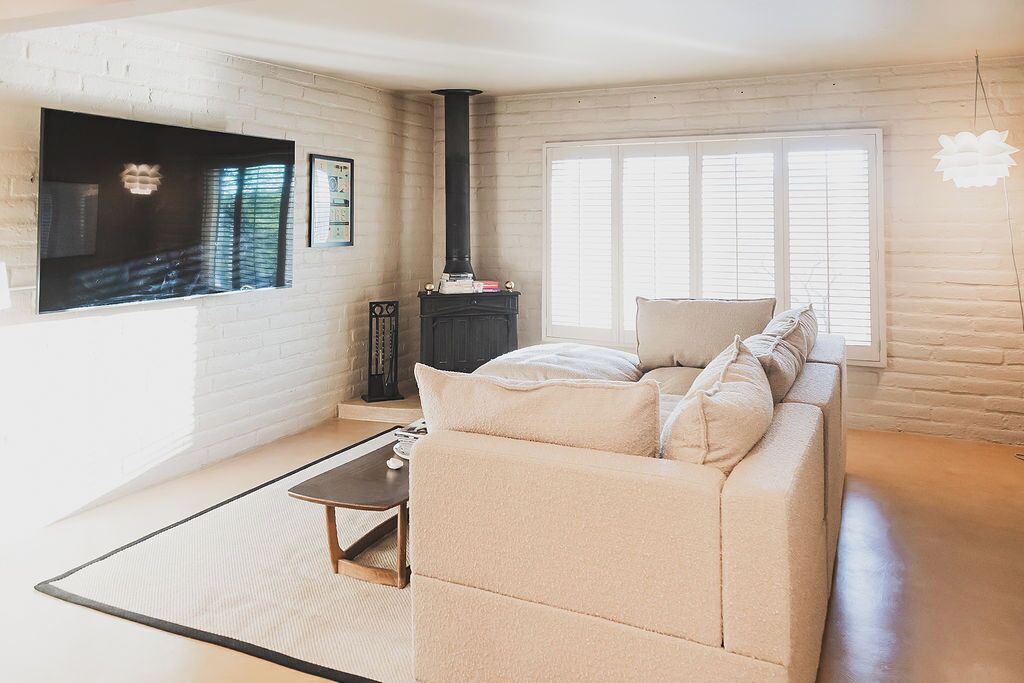 Een woonkamer met een bank, een open haard, een aan de muur bevestigde televisie en een raam met zonwering.
