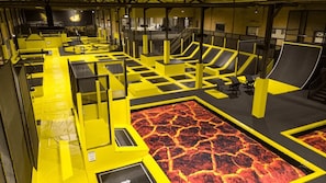 An indoor trampoline park with yellow and black safety barriers, a lava-themed floor, and seating areas. - Schotte Youth Accommodation Centre (Aalst)