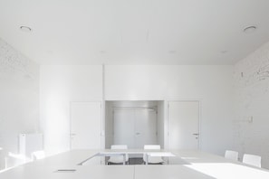 A conference room with a long table and chairs, white brick walls, and a door with a handle. - Schotte Youth Accommodation Centre (Aalst)