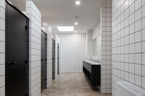 A modern bathroom with white tiled walls, a central sink area, and a skylight. - Schotte Youth Accommodation Centre (Aalst)